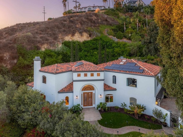 mediterranean / spanish home featuring a lawn, solar panels, and french doors