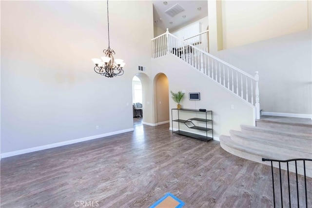 stairway featuring wood-type flooring, a towering ceiling, and an inviting chandelier