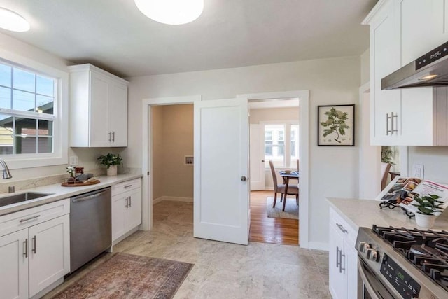 kitchen with white cabinets, appliances with stainless steel finishes, wall chimney range hood, and sink