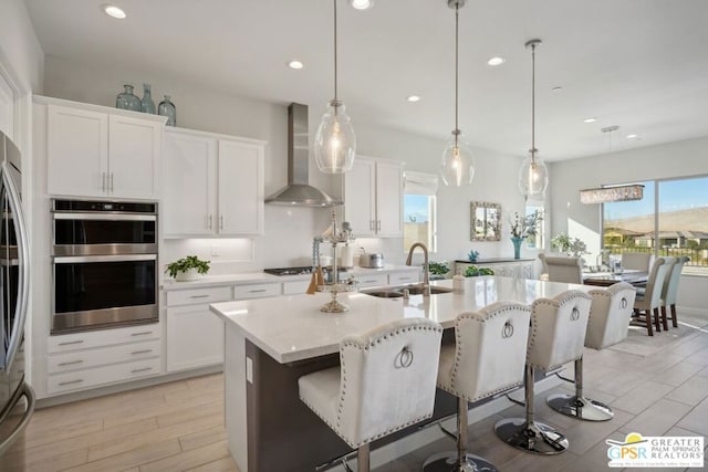 kitchen with decorative light fixtures, wall chimney exhaust hood, a kitchen bar, and a kitchen island with sink