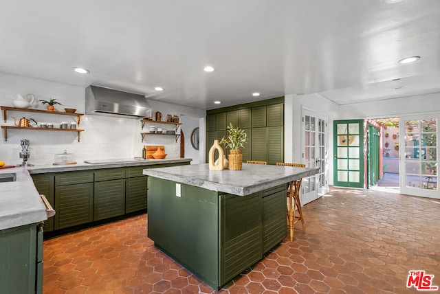 kitchen featuring french doors, green cabinets, wall chimney range hood, decorative backsplash, and a kitchen island