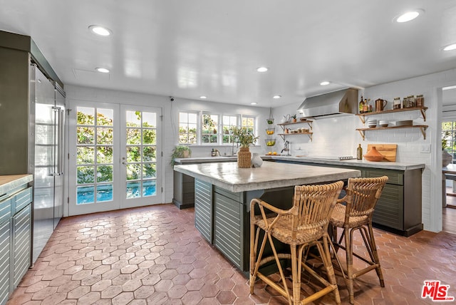 kitchen featuring a kitchen breakfast bar, a kitchen island, wall chimney range hood, and a healthy amount of sunlight