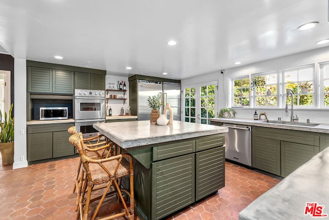 kitchen with appliances with stainless steel finishes, a kitchen breakfast bar, green cabinets, and sink