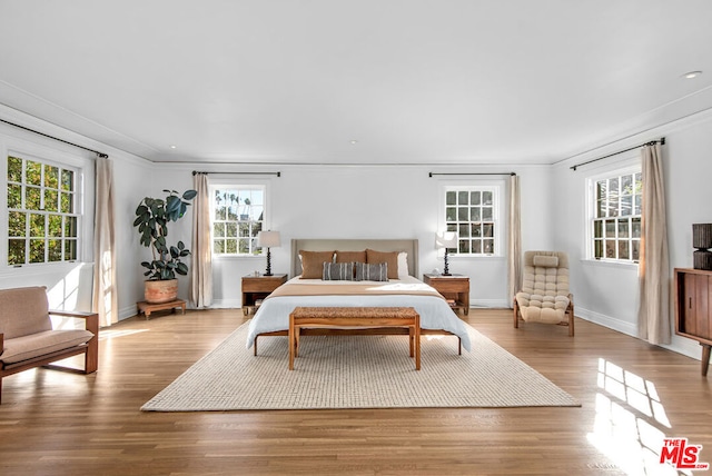 bedroom featuring light hardwood / wood-style floors, multiple windows, and crown molding