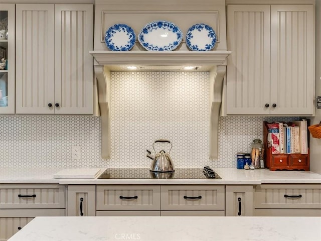 kitchen featuring tasteful backsplash, light stone countertops, and black electric stovetop