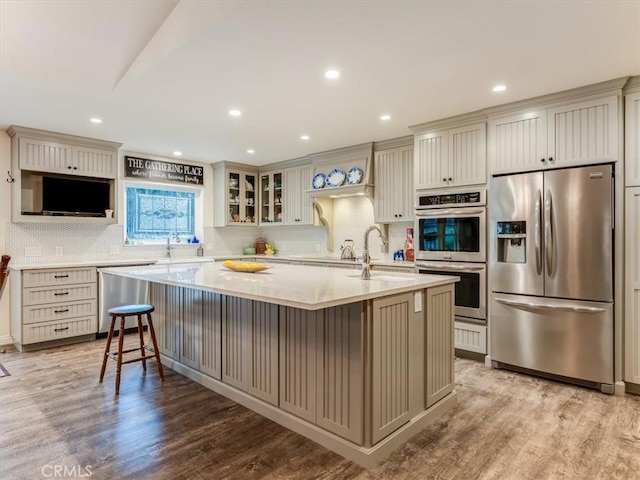 kitchen with a center island with sink, sink, light wood-type flooring, appliances with stainless steel finishes, and a breakfast bar area