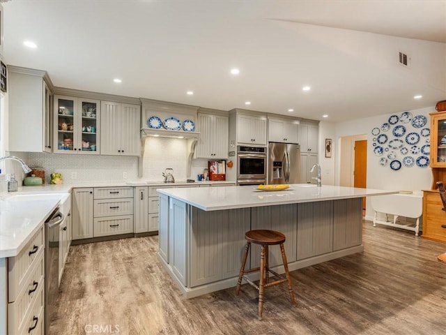 kitchen featuring a breakfast bar, sink, light wood-type flooring, an island with sink, and appliances with stainless steel finishes