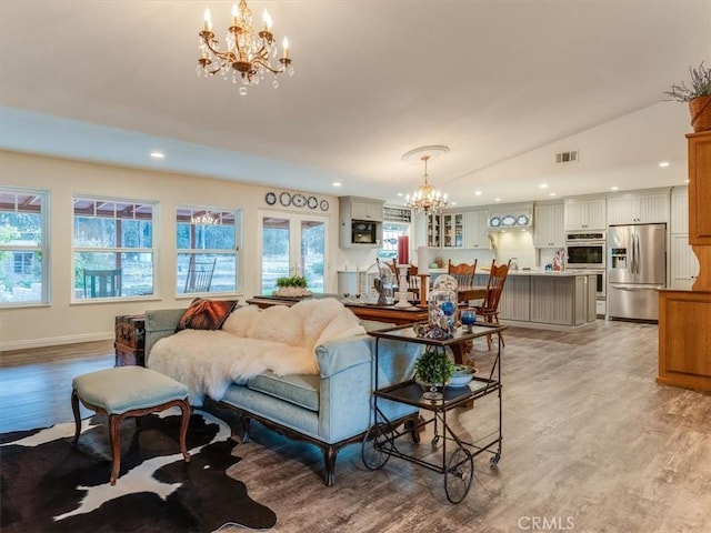 living room with light wood-type flooring, an inviting chandelier, vaulted ceiling, and plenty of natural light