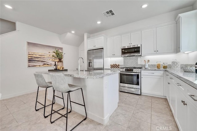 kitchen with a kitchen island with sink, white cabinets, stainless steel appliances, and light stone counters