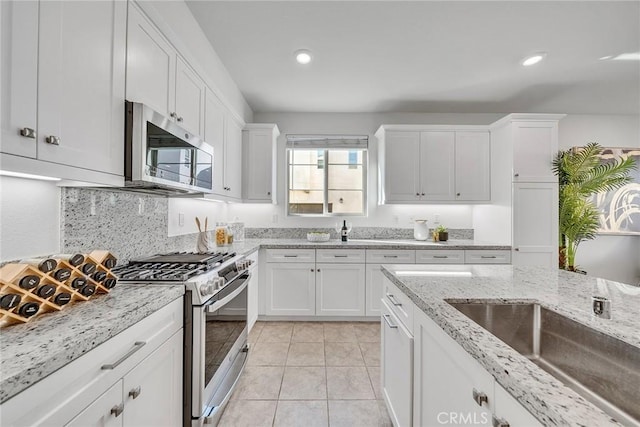 kitchen with tasteful backsplash, light stone counters, stainless steel appliances, sink, and white cabinetry