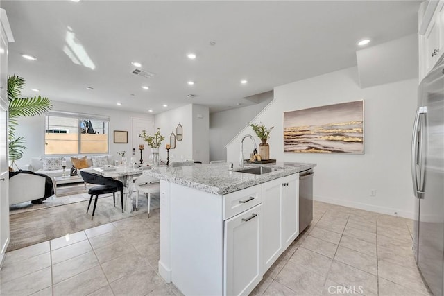 kitchen with a center island with sink, light stone counters, white cabinetry, and stainless steel appliances