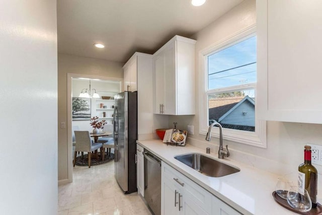 kitchen with pendant lighting, white cabinets, sink, appliances with stainless steel finishes, and a chandelier