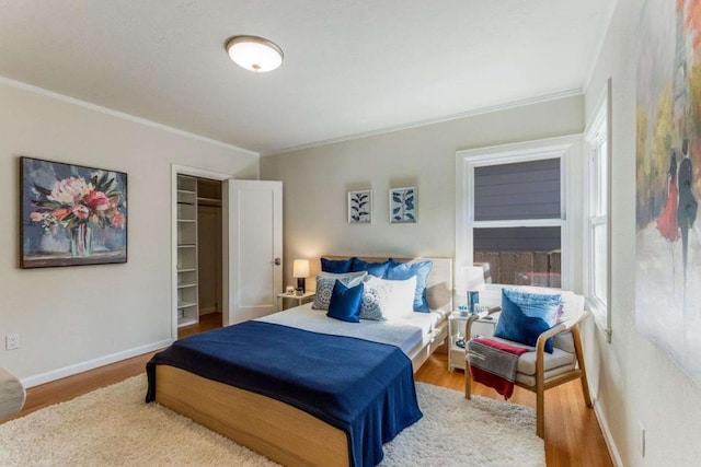 bedroom with wood-type flooring, a walk in closet, a closet, and ornamental molding