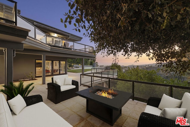 patio terrace at dusk featuring a balcony and an outdoor living space with a fire pit