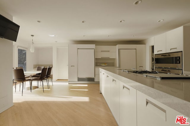 kitchen featuring white cabinets, light hardwood / wood-style floors, hanging light fixtures, and appliances with stainless steel finishes