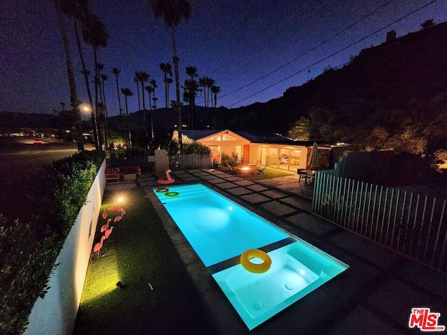 pool at night featuring an in ground hot tub and a patio