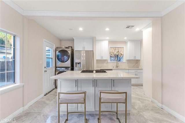 kitchen with visible vents, a kitchen island, appliances with stainless steel finishes, white cabinets, and stacked washer / dryer