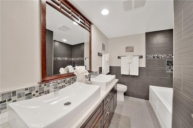 bathroom featuring toilet, vanity, tile walls, and a bath