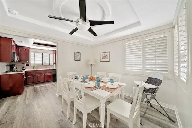 dining space featuring a healthy amount of sunlight, light hardwood / wood-style flooring, sink, and a tray ceiling