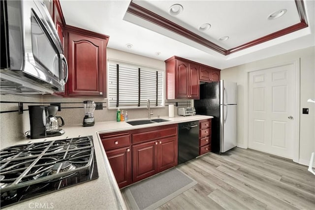 kitchen featuring stainless steel appliances, backsplash, sink, light hardwood / wood-style floors, and a tray ceiling