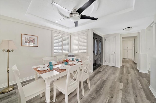 dining space featuring light hardwood / wood-style floors, ceiling fan, and a tray ceiling