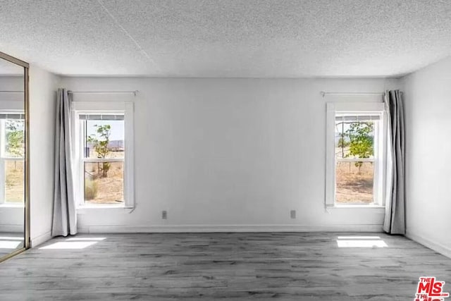 unfurnished room featuring wood-type flooring, a textured ceiling, and plenty of natural light