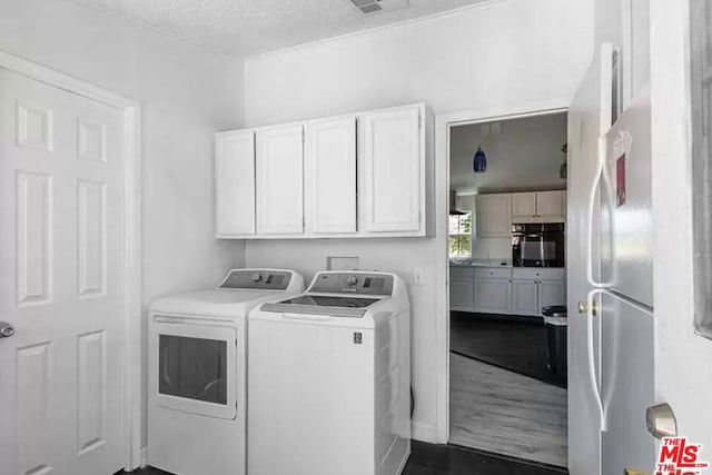 clothes washing area with cabinets, a textured ceiling, washing machine and dryer, and dark hardwood / wood-style flooring