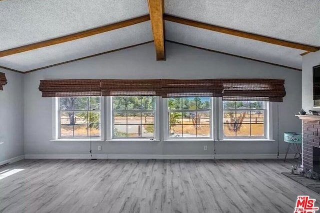 unfurnished living room featuring a textured ceiling, lofted ceiling with beams, light hardwood / wood-style flooring, and a brick fireplace