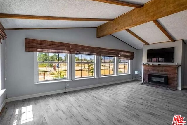 unfurnished living room with vaulted ceiling with beams, a brick fireplace, a textured ceiling, and hardwood / wood-style flooring