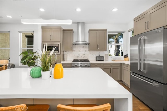 kitchen featuring hardwood / wood-style floors, backsplash, a kitchen breakfast bar, wall chimney exhaust hood, and stainless steel appliances