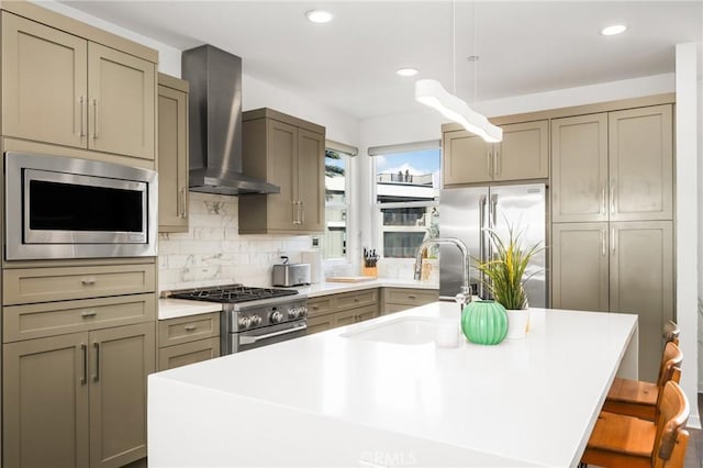 kitchen featuring pendant lighting, sink, wall chimney exhaust hood, premium appliances, and a breakfast bar area