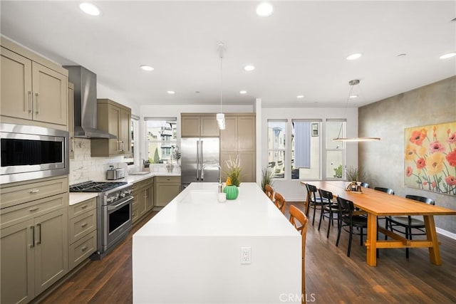 kitchen with pendant lighting, a center island with sink, wall chimney range hood, dark hardwood / wood-style floors, and appliances with stainless steel finishes