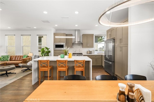 kitchen with a center island, stainless steel appliances, wall chimney range hood, dark hardwood / wood-style floors, and a breakfast bar area