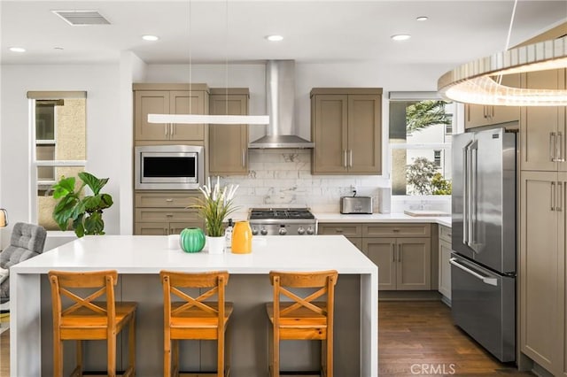 kitchen featuring a kitchen breakfast bar, wall chimney range hood, dark hardwood / wood-style floors, decorative backsplash, and appliances with stainless steel finishes