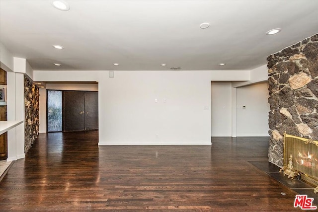 unfurnished living room featuring a stone fireplace and dark wood-type flooring