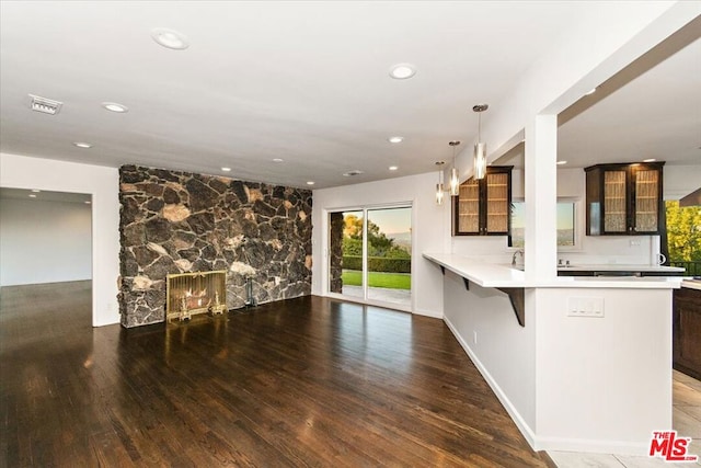 kitchen with kitchen peninsula, a breakfast bar, pendant lighting, dark hardwood / wood-style floors, and a stone fireplace