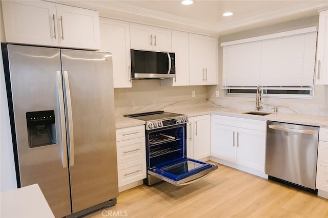 kitchen with white cabinets, ornamental molding, stainless steel appliances, and light hardwood / wood-style flooring