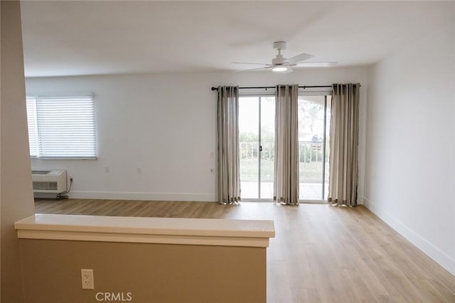 empty room featuring ceiling fan, light wood-type flooring, and a wall unit AC