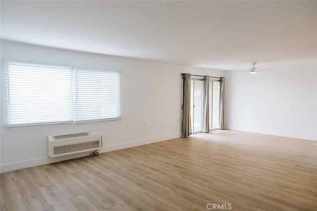 empty room featuring a wall unit AC, ceiling fan, and light wood-type flooring