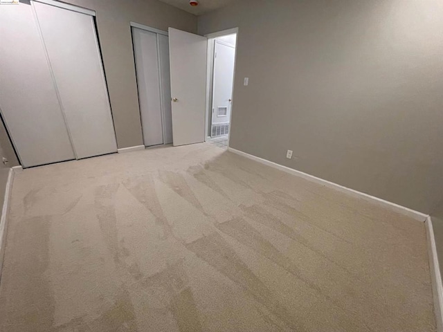 unfurnished bedroom featuring light carpet and two closets