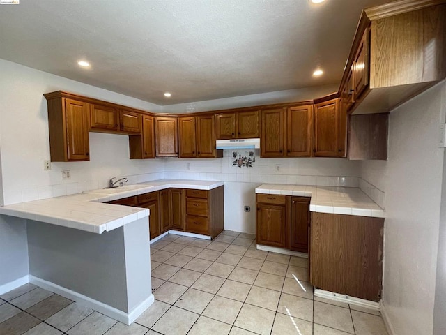 kitchen featuring tile countertops, light tile patterned flooring, kitchen peninsula, and sink