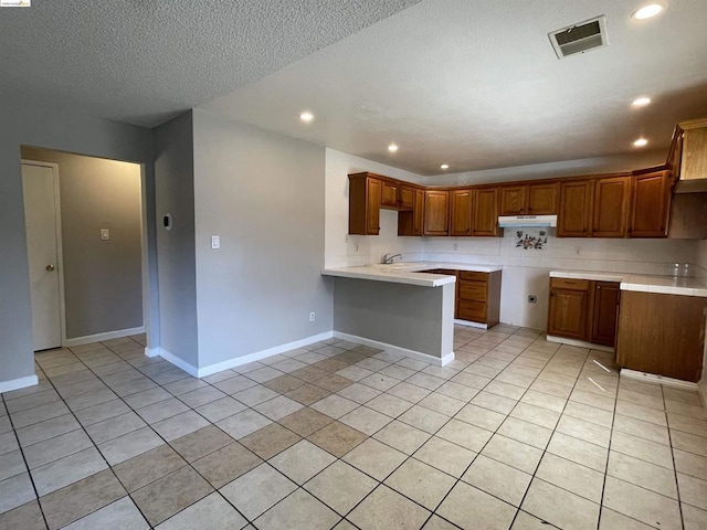 kitchen featuring kitchen peninsula, light tile patterned floors, a textured ceiling, and sink