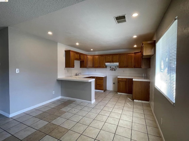 kitchen with kitchen peninsula, a textured ceiling, and light tile patterned floors