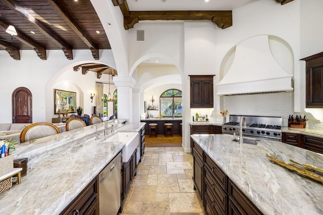 kitchen featuring sink, stainless steel appliances, light stone countertops, custom range hood, and beamed ceiling