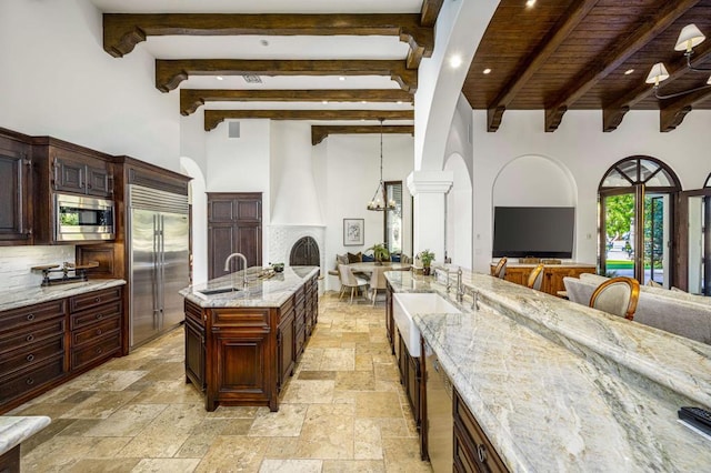 kitchen featuring pendant lighting, an inviting chandelier, built in appliances, light stone counters, and a kitchen island