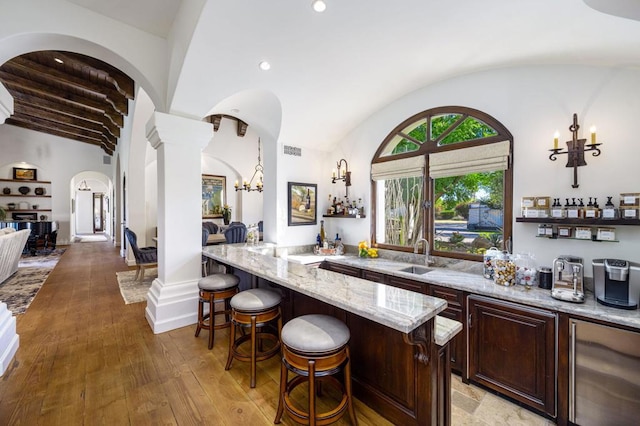 bar with vaulted ceiling, decorative light fixtures, decorative columns, light stone countertops, and light wood-type flooring