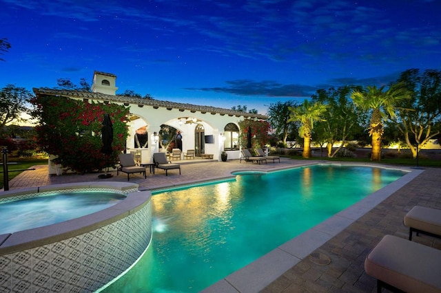 pool at dusk featuring a patio area and an in ground hot tub