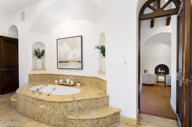 bathroom featuring a relaxing tiled tub and a fireplace