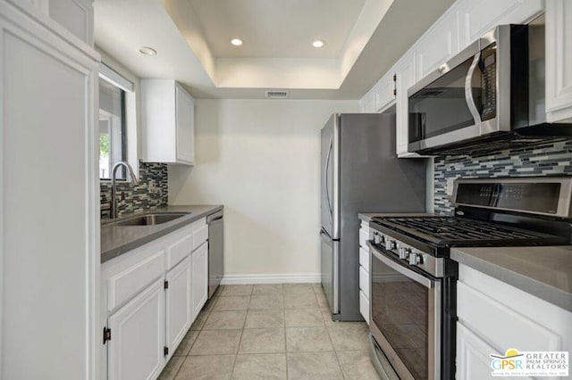 kitchen featuring backsplash, a raised ceiling, sink, appliances with stainless steel finishes, and white cabinetry