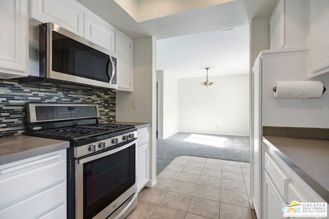 kitchen featuring tasteful backsplash, white cabinetry, stainless steel appliances, and decorative light fixtures